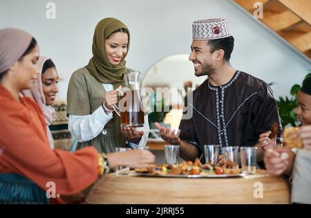 Gruppe muslimischer Menschen, die Eid oder Ramadan mit iftar zu Hause mit Essen, Trinken und Familie feiern. Junge Islamfrau gießt Saft für ein glückliches, lächelndes Stockfoto