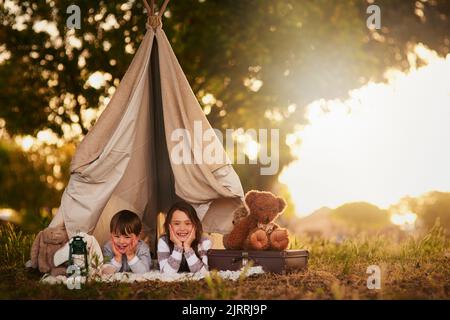 Lassen Sie sich von uns informieren, wenn Sie das Passwort kennen. Portrait von zwei niedlichen kleinen Geschwistern, die draußen in einem Tipi spielen. Stockfoto