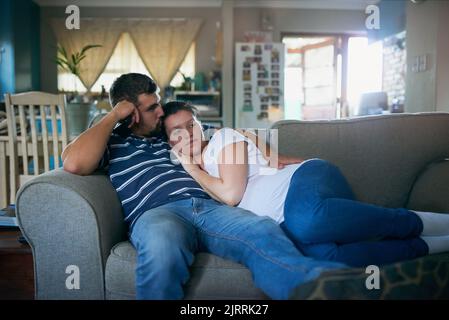 Sie haben ein glückliches Leben zusammen gebaut. Ein liebevolles, trächtiges Paar, das sich zu Hause auf der Couch entspannt. Stockfoto