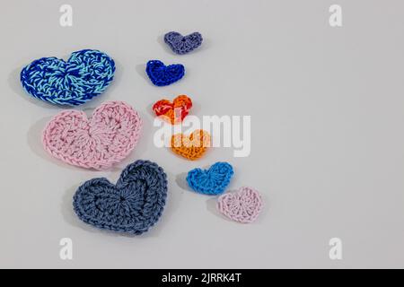 Set von handgefertigten Häkelherzen in verschiedenen Farben und Größen auf weißer Oberfläche und Hintergrund, in blau, rosa, orange, grau und gemischten Farben. Handgefertigte c Stockfoto