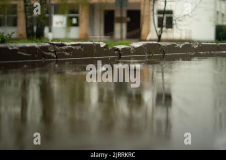 Regen draußen. Große Pfütze im Hof. Nasses Wetter. Oberfläche der Pfütze. Wasser auf der Straße. Stockfoto