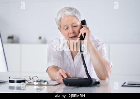 Geschäftsfrau, die am Schreibtisch im Büro einen Anruf über das Festnetztelefon tätigen kann Stockfoto