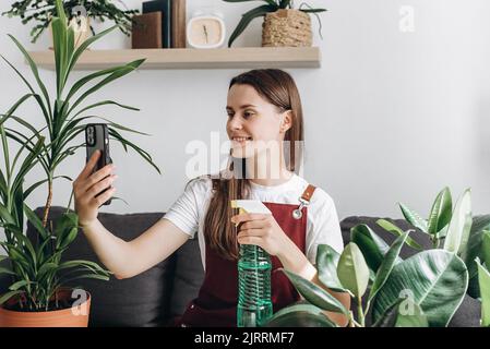 Lächelndes Gärtnermädchen, das angenehme Unterhaltung mit einer mobilen Webcam-Videoanruf-Anwendung während der Transplantation von Innenpflanzen genießt. Konzept Werk ca. Stockfoto