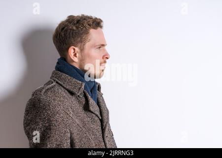 Portrait schöner bärtiger Mann im Mantel mit Schal, männliche Schönheit, saisonale Mode. Studio auf einem hellen Hintergrund aufgenommen Stockfoto
