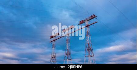 Hochspannungsleitungen und Strommasten bei Sonnenuntergang. Landschaft mit Wolken und blauem Himmel. Stockfoto