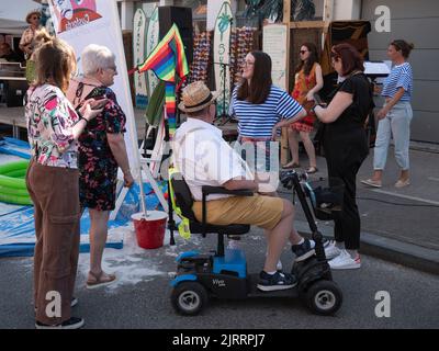 Sint Gillis Waas, Belgien, 06. August 2022, ein älterer Mann mit einem Mobilitätsroller hat ein Gespräch mit ein paar Damen Stockfoto