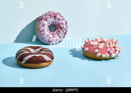 Drei süße leckere Donuts in Karamell- und Schokoladenglasur, auf zweifarbigem Hintergrund Stockfoto