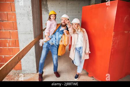 Mann hält Tochter und lächelt. Glückliches Paar Immobilienkäufer demonstrieren Schlüssel von neuem Haus im Bau. Familienleben und neues Hauskauf-Konzept. Stockfoto