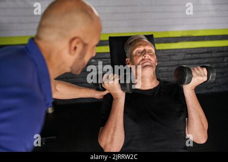 Männliche Personal Trainer und reifen Mann tun ........ Übung mit Hanteln und Bank Stockfoto