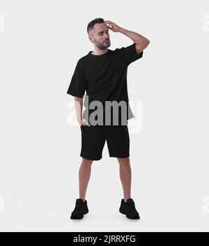 Übergroße schwarze Anzug Mockup auf einem bärtigen Kerl in Turnschuhen Fixierung seine Haare isoliert auf dem Hintergrund. T-Shirt-Vorlage mit lockerer Passform, Shorts auf einem Mann, Klo Stockfoto