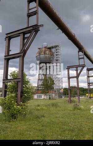 Eine Vertikale eines alten industriellen Wasserturms, der an einem bewölkten Tag von rostigen Rohrleitungen umgeben ist Stockfoto