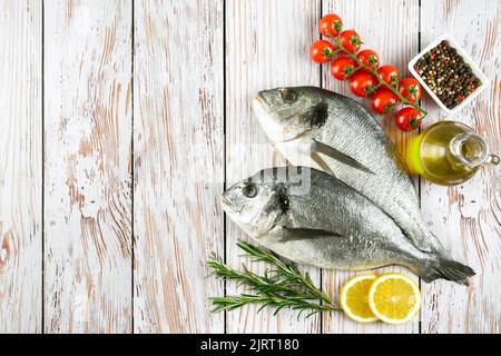 Roher Fisch dorado auf weißem Holzhintergrund mit Gewürzen, Tomaten, Rosmarin, Olivenöl und Zitrone. Draufsicht, flach liegend mit Platz für Text Stockfoto