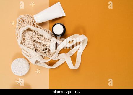 Ein Layout für Ihr Naturkosmetik-Produkt und eine Kopierfläche für Ihre Werbung. Cremefarbenes, grünes Blatt, eine Tube Creme, ein Netzbeutel auf hellbeigem Hintergrund. Stockfoto