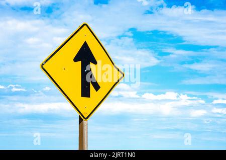 Ein gelbes Straßenschild in Amerika vor einem blauen Himmel mit Wolken, die darauf hinweisen, dass die Fahrspuren vor uns zusammenfließen werden. Stockfoto