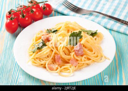 Pasta Carbonara mit Schinken und Parmesan serviert auf einem weißen Teller auf einem blauen Holztisch. Draufsicht, flach liegend Stockfoto