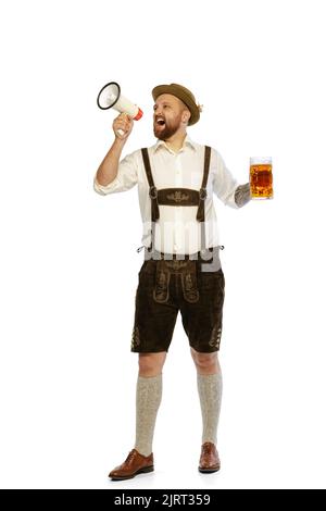 Porträt eines jungen Mannes in traditioneller bayerischer oder deutscher Kleidung, der in einem Megaphon auf weißem Hintergrund schreit Stockfoto