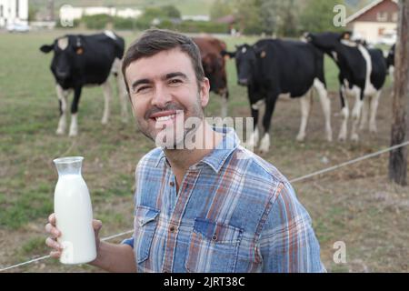 Bauer hält frische Milch mit Kühen im Hintergrund Stockfoto