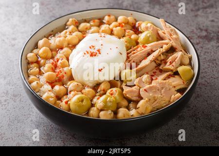 Lablabi Tunisian Spicy Chickpea Eintopf mit grüner Olive, Thunfisch aus der Dose und pochiertem Ei aus der Nähe in der Schüssel auf dem Tisch. Horizontal Stockfoto