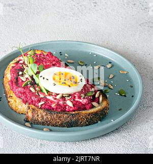 Vollkorn-Toast mit Rübenhummus, Samen, Ei und Mikrogemüse (gekeimt Erbsensprossen) auf hellgrauem Hintergrund. Das Konzept der gesunden Ernährung.. Stockfoto