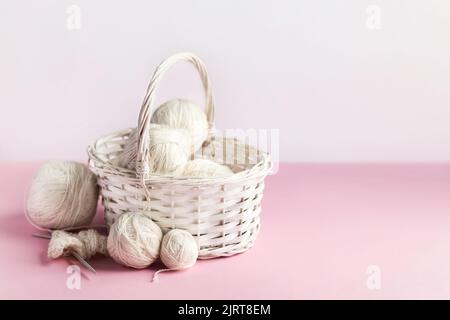 Weiße Garnbälle in einem Korb auf einem rosa Hintergrund zum Stricken warmer Kleidung und Hobbys Handarbeiten Stockfoto