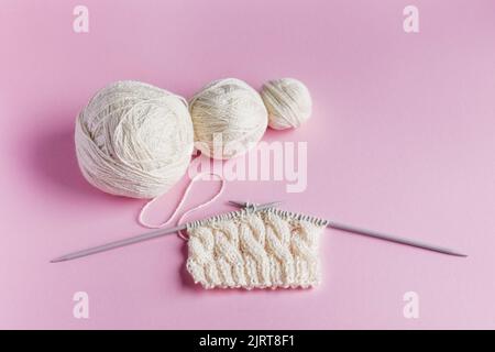 Weiße Garnbälle mit Stricknadeln in einem Saitenbeutel auf fliederem Hintergrund zum Stricken warmer Kleidung, Hobbys Stockfoto