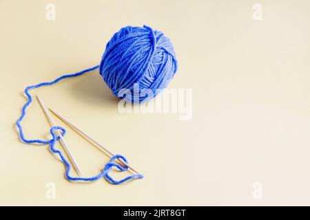 Blauer Ball aus Strickfäden mit Stricknadeln auf gelbem Hintergrund zum Stricken warmer Kleidung Stockfoto