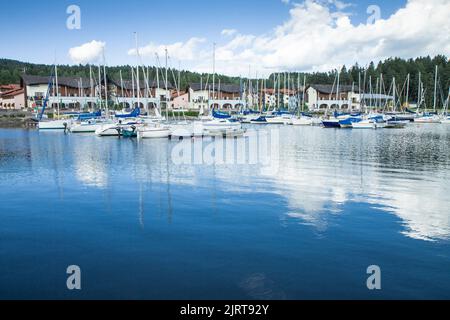 Wunderschöne Aussicht auf Segelboote, die sich auf der Wasseroberfläche spiegeln. Schöner moderner Hafen im Hintergrund. Lipno nad Vltavou, Tschechische Republik. Unglaublich sonniger Tag Stockfoto