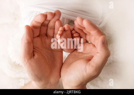 Die Füße der Kinder in den Händen von Mutter und Vater. Mutter, Vater und Kind. Stockfoto