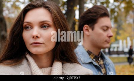 Kaukasisches Mädchen beleidigt von männlichen Liebhaber auf Hintergrund junge Familie Paar im Freien stehend ignorieren einander suchen verschiedene Wege Konflikt Stockfoto