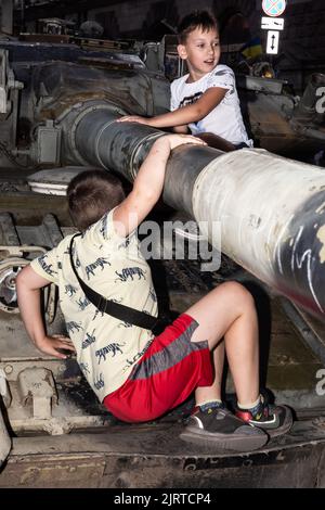 KIEW, UKRAINE - 24. August 2022: Die Jungen spielen auf einem ausgebrannten russischen Panzer. Der Unabhängigkeitstag der Ukraine. Auf Chreschtschatyk in Kiew wird eine Ausstellung zerstörter russischer Waffen organisiert Stockfoto