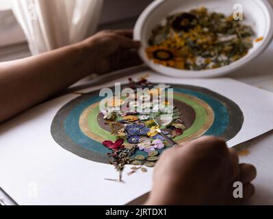Frau, die Innendekoration mit gepressten Blumen und Blättern auf Leinwand mit Acrylfarbe Kreise. Pressen Blume Moderne Kunst. Stockfoto