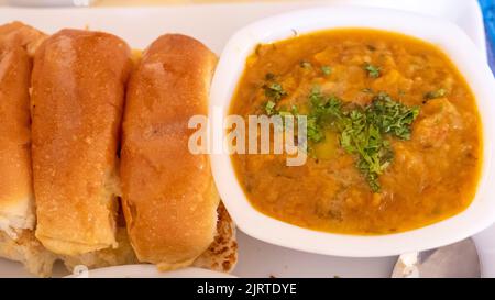 PAV Bhaji Fast-Food-Gericht aus Indien. Besteht aus einem dicken Gemüsearschrot, serviert mit einem weichen Brötchen, serviert auf einem Teller. Stockfoto