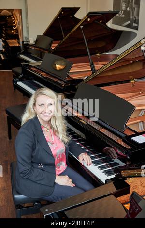 Hamburg, Deutschland. 25. August 2022. Yvonne Trübger, Inhaberin, sitzt während einer Fotosession am Flügel, um das 150.-jährige Jubiläum des Pianohaus Trübger zu feiern. Das Klavierhaus ist eines der letzten Klavierhäuser, das nicht nur eine Marke repräsentiert. (To dpa 'Pianohaus Trübger verschenkt 15 Klaviere zum 150.-jährigen Jubiläum') Quelle: Georg Wendt/dpa/Alamy Live News Stockfoto