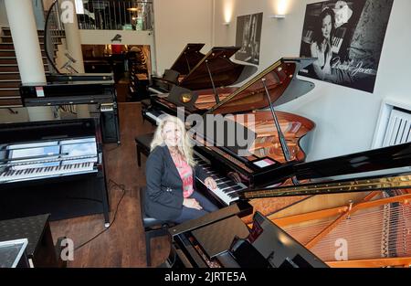 Hamburg, Deutschland. 25. August 2022. Yvonne Trübger, Inhaberin, sitzt während einer Fotosession am Flügel, um das 150.-jährige Jubiläum des Pianohaus Trübger zu feiern. Das Klavierhaus ist eines der letzten Klavierhäuser, das nicht nur eine Marke repräsentiert. (To dpa 'Pianohaus Trübger verschenkt 15 Klaviere zum 150.-jährigen Jubiläum') Quelle: Georg Wendt/dpa/Alamy Live News Stockfoto