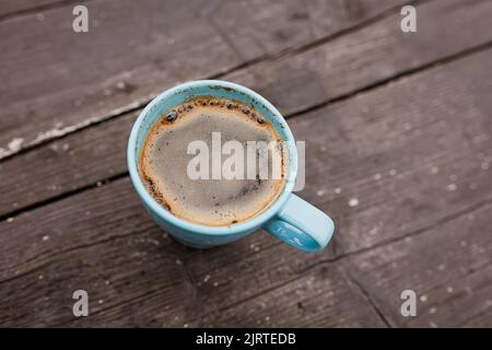 Türkisfarbener Becher mit Kaffee auf dunklem Holzhintergrund Stockfoto