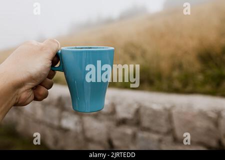 Türkisfarbener Becher mit Kaffee auf dem Hintergrund einer Bergwiese Stockfoto