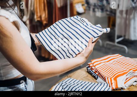 Moderne Latina junge Frau Wahl 100 Prozent Bio-Baumwolle tragen T-Shirt in modernen umweltfreundlichen Shop Stockfoto