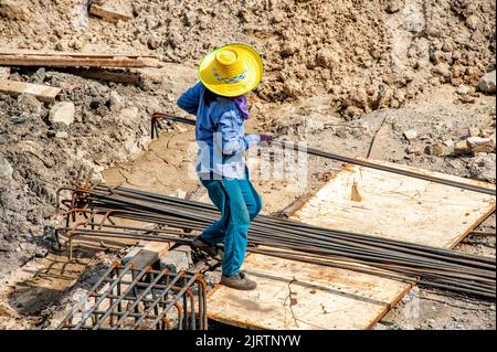 Ein Bauarbeiter trägt an einem sehr heißen Tag verformte Stäbe für die Fundamentstahlarbeiten. Stockfoto