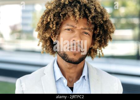 Nahaufnahme eines stolzen selbstbewussten, eleganten, lockigen brasilianischen oder hispanischen Mannes, erfolgreicher Unternehmer, Geschäftsmann, der im Freien steht und die Kamera anschaut Stockfoto