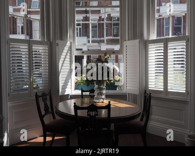 Blumenvase auf Holztisch in teilweisem Sonnenlicht durch Holzjalousien Stockfoto