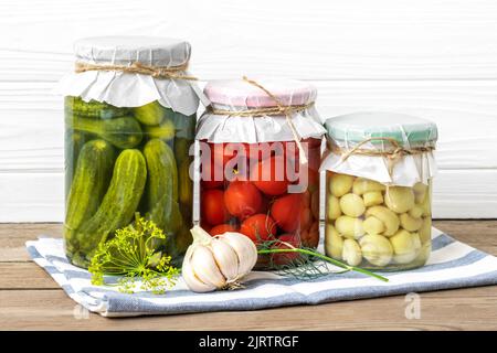 Hausgemachte eingelegte Kirschtomaten, Gurken, Champignons, Knoblauch, Auberginen, Rote Paprika in Gläsern auf Holzregal hausgemachte Konserven und fermentierte Lebensmittel Konzept Saisonprodukt. Stockfoto