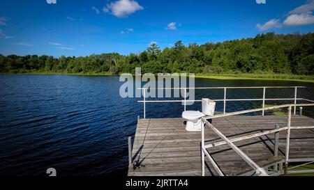 Ein Angelstock und eine Toilette sitzen auf einem hölzernen Pier am Gass Lake in der Nähe von Manitowoc, Wisconsin. Stockfoto