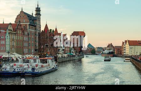 Ein Bild von einigen Danziger Sehenswürdigkeiten neben dem Fluss Motlawa, wie dem Kranich, dem Marien-Tor und dem Schiff der Schwarzen Perle, bei Sonnenuntergang. Stockfoto