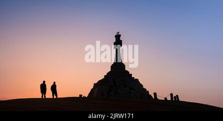 Ein Panoramabild der Silhouette zweier Menschen, die bei Sonnenuntergang in Cornwall im Vereinigten Königreich neben dem imposanten Newquay war Memorial stehen. Stockfoto