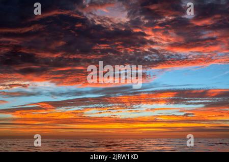 Ein wunderschöner und ungewöhnlicher Sonnenuntergang mit dunklen Wolken, gemischt mit leuchtend orangefarbenen Sonneneinstrahlung über dem Pazifischen Ozean. Stockfoto