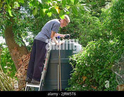 Mann, der den Füllstand des inländischen Heizöl-Tanks im Garten vereinigtes Königreich überprüft Stockfoto