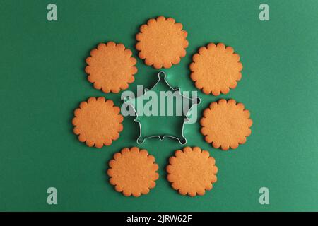Weihnachts-Lebkuchenkekse und Metallic-Ausstechform auf grünem Hintergrund angeordnet. Draufsicht. Stockfoto