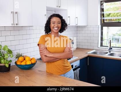 Eine junge, multiethnische Frau steht mit gekreuzten Armen in einer sauberen Küche Stockfoto