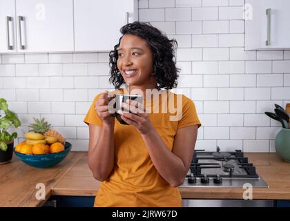 Eine junge, multiethnische Frau trinkt gerne Kaffee in einer hellen, modernen Küche Stockfoto