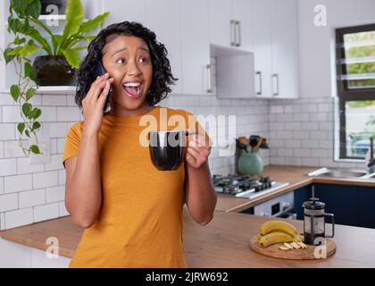 Eine junge Frau ist überrascht und glücklich über einen Anruf in der Küche Stockfoto